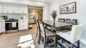 A modern kitchen with a dining area, featuring a large wooden table, white chairs, and a potted plant. - 13 Mi to Lumen Field & Dtwn Seattle! Cozy Retreat (Newcastle)