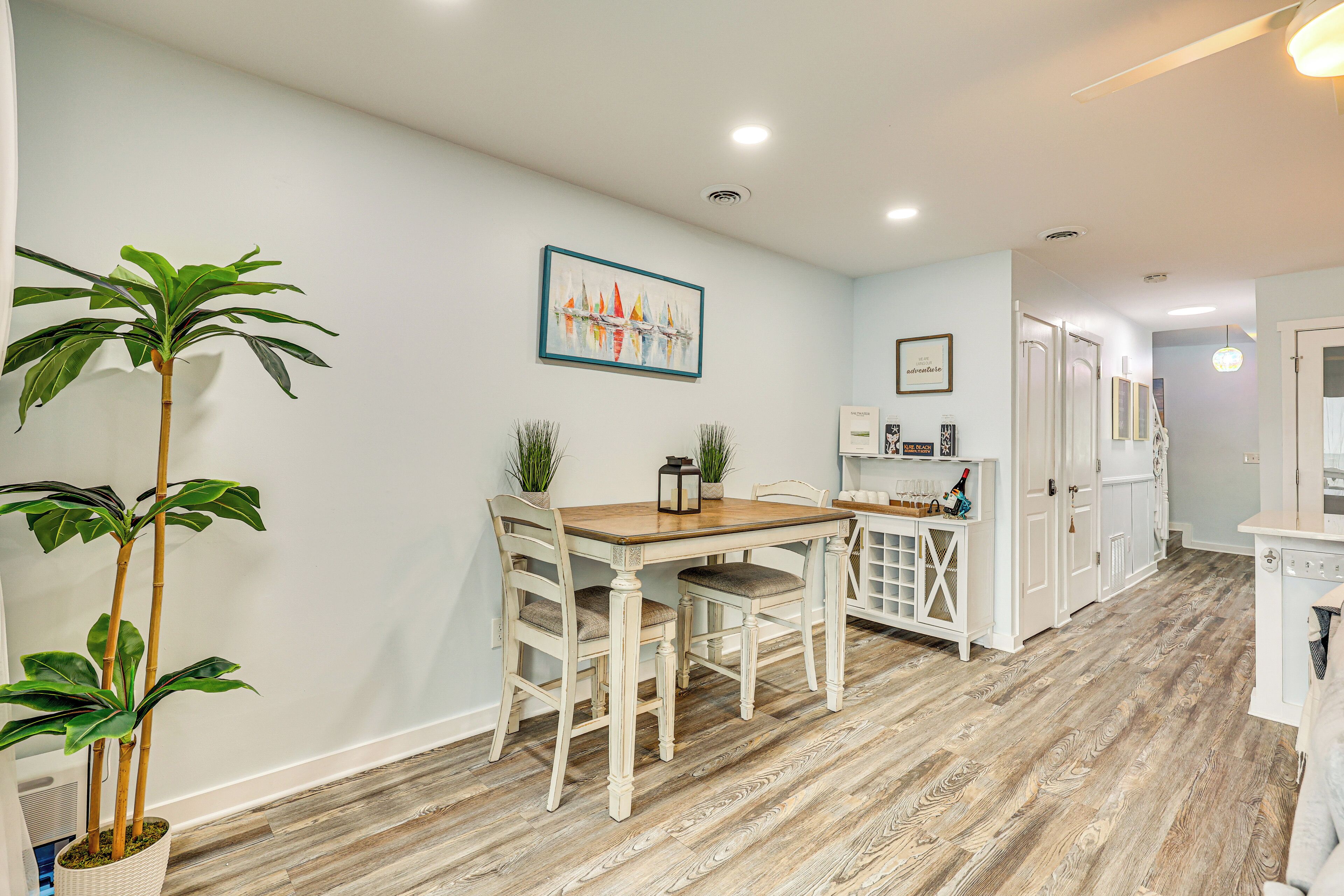 A dining area with a wooden table and chairs, a potted plant, and a painting on the wall.