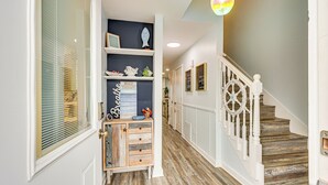 A hallway with a wooden floor, white railing, and a door with a window. - Poolside Fun + Oceanfront Bliss: Kure Beach Haven! (Kure Beach)