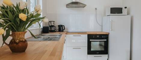 Une cuisine moderne avec des armoires blanches, un plan de travail en bois, un four encastré, un four à micro-ondes et un vase rempli de tulipes jaunes.