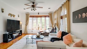A living room with a flat-screen TV, a ceiling fan, a sofa, a coffee table, and a window with curtains. - Take Metro to DC! Family Home in Springfield (Springfield)