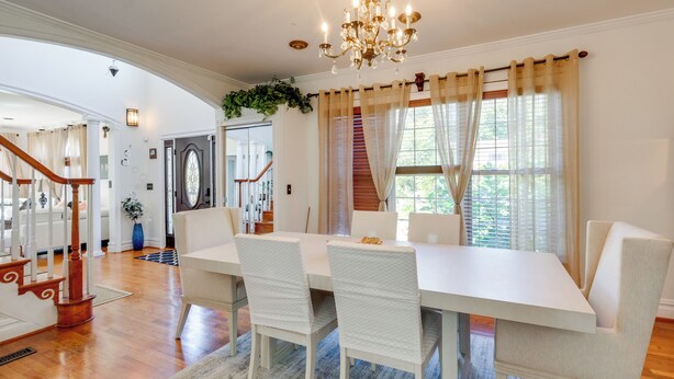 A dining area with a white table and chairs, a chandelier, and a staircase in the background. - Take Metro to DC! Family Home in Springfield (Springfield)