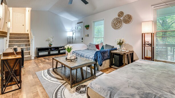 Ein geräumiges Wohnzimmer mit Deckenventilator, einer Treppe, einer Couch, einem Couchtisch und einem großen Fenster mit Jalousien.