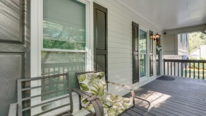 Eine Veranda mit einer hölzernen Bank und einem Stuhl, ein Fenster mit Jalousien und eine Tür mit einer Zierverkleidung.