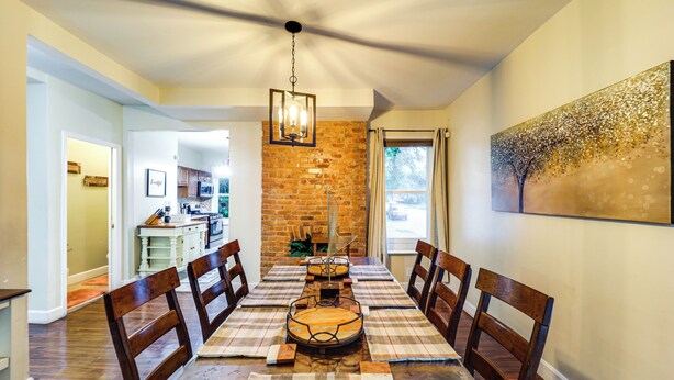 Un coin repas avec un mur en briques, un lustre et un grand tableau accroché au mur.
