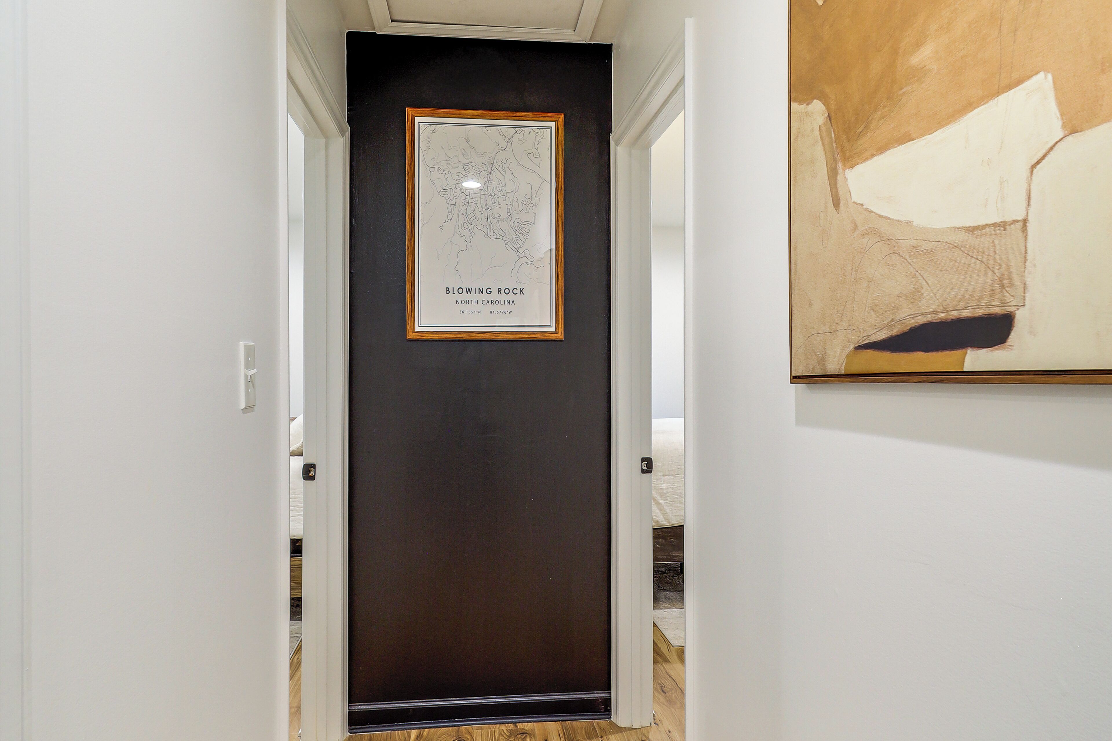 A hallway with a framed map of Blowing Rock, North Carolina, and a partial view of a painting on the right wall.