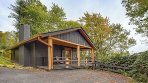A cabin with a wooden deck, a chimney, and a porch.