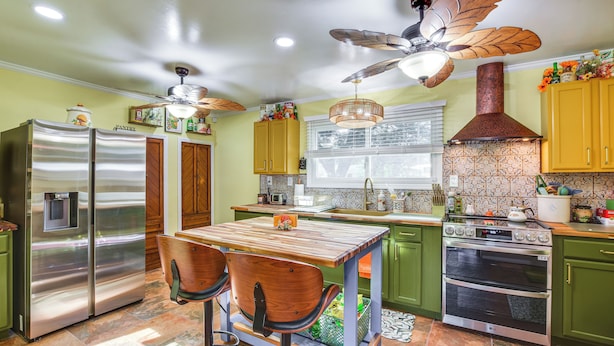 Une cuisine avec une table en bois, deux chaises, un réfrigérateur en acier inoxydable, un four à micro-ondes, une cuisinière et un ventilateur de plafond.