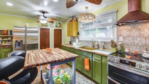 Une cuisine avec une table en bois, des placards verts, un réfrigérateur en acier inoxydable et une cuisinière.