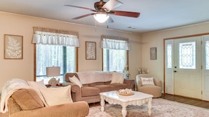 A living room with a brown sofa, a white coffee table, and a ceiling fan. - Forested Family Hideaway Near Lake Sinclair! (Eatonton)