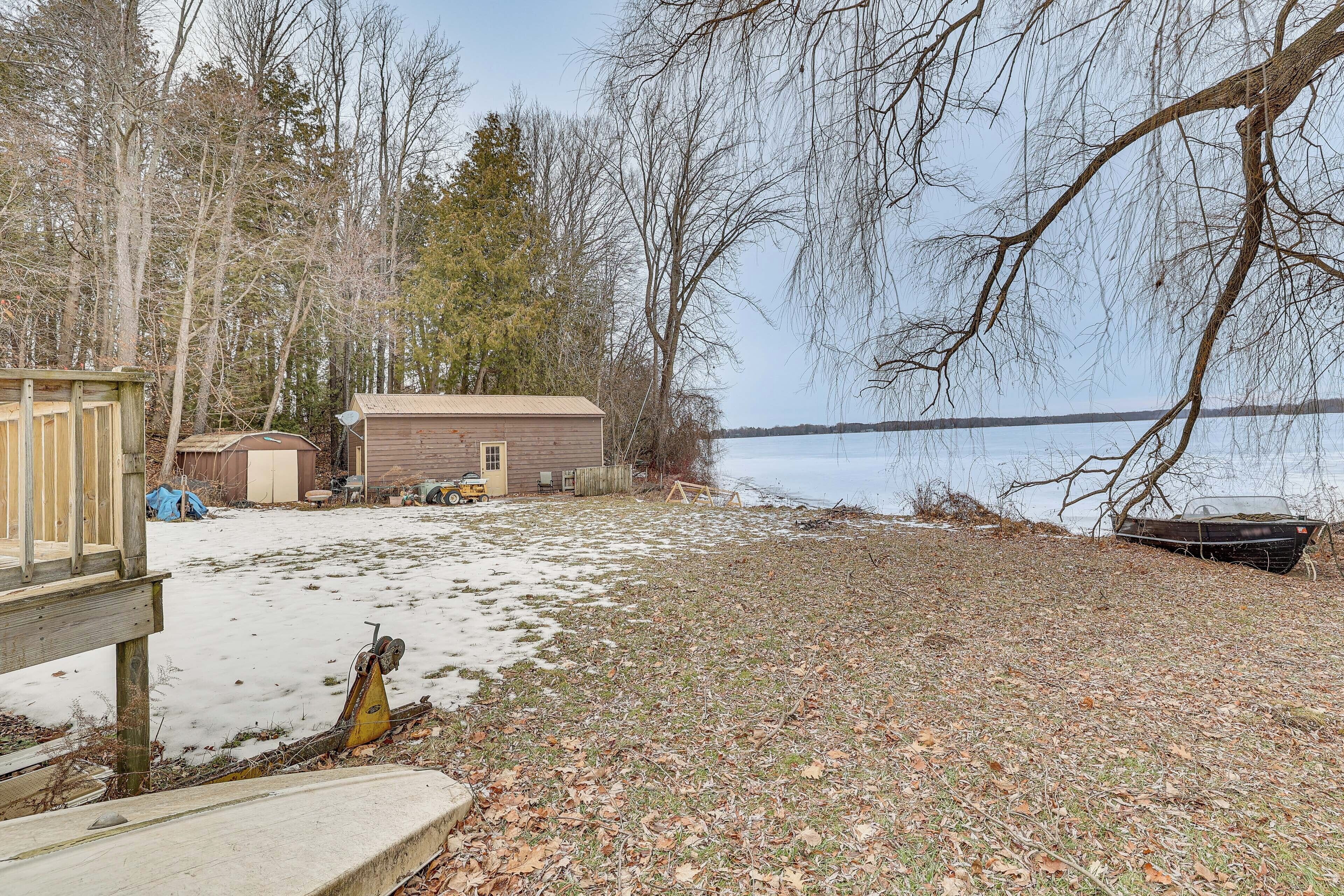 A cabin with a dock by a lake, surrounded by trees and a snowy ground.