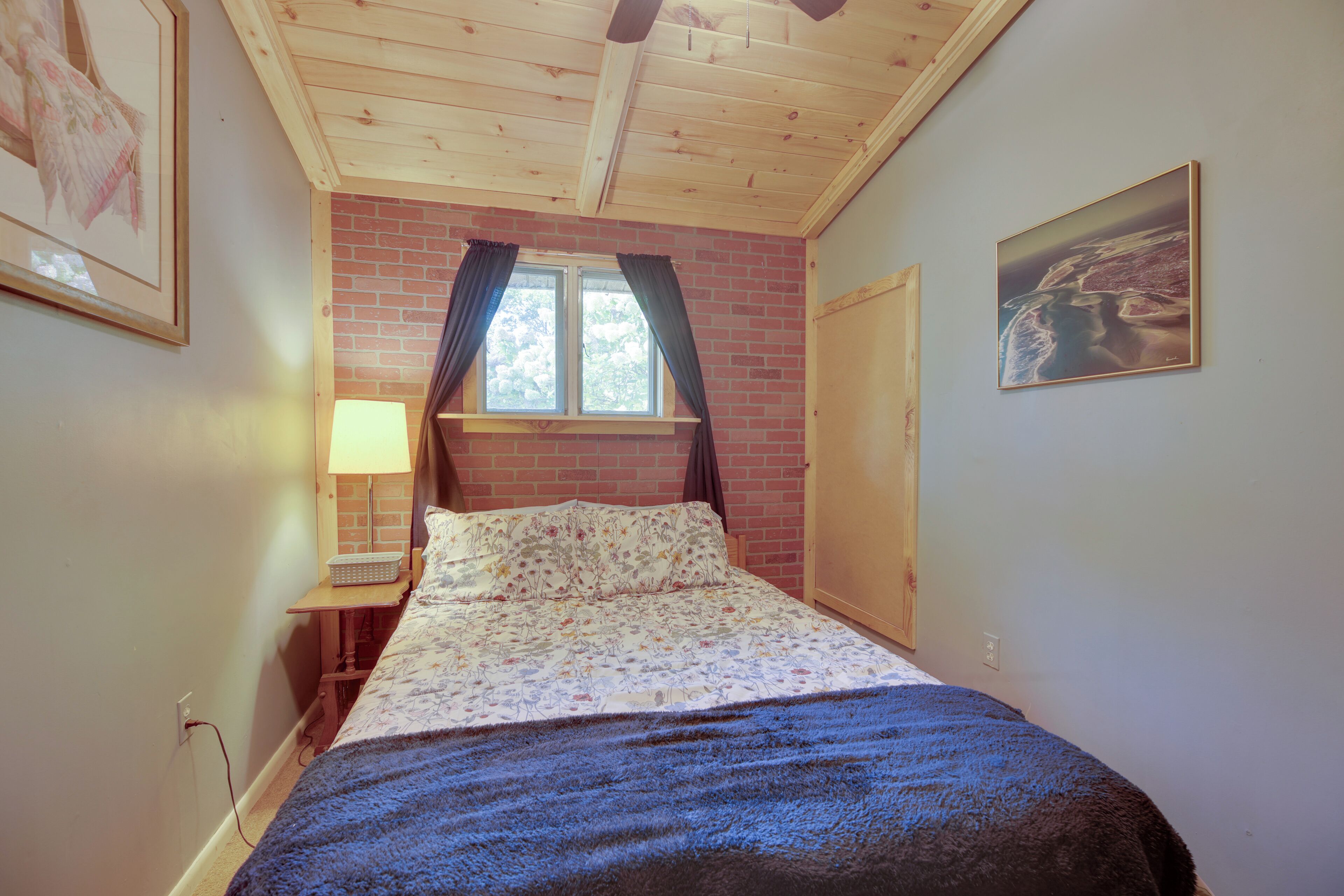 A bedroom with a bed, a window with curtains, a lamp, and a painting on the wall.