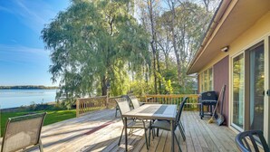 Una terraza de madera con una mesa y sillas, con vistas a un lago y rodeada de árboles.