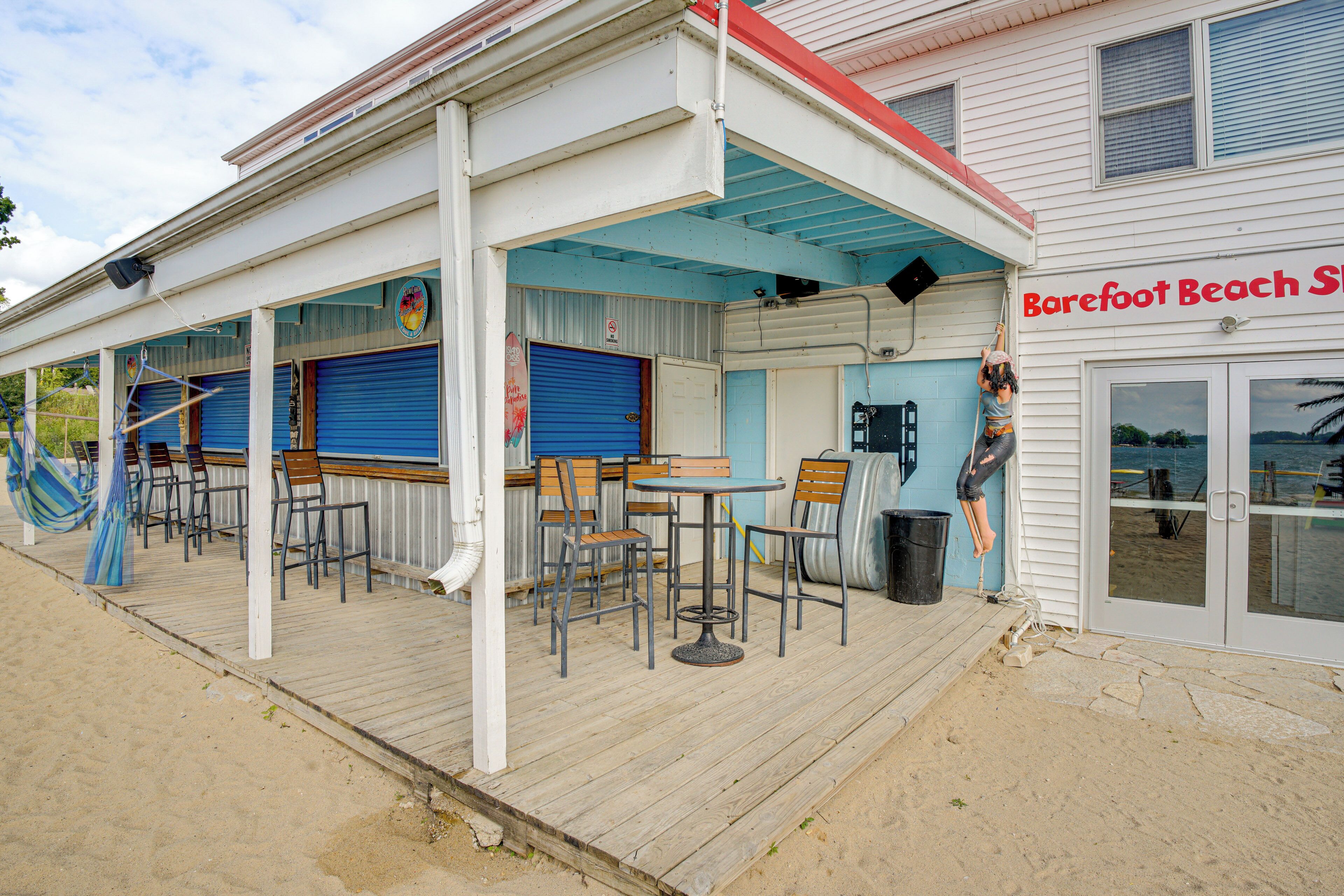 Een gebouw aan het strand met een overdekt terras, buiten zitplaatsen en een bord waarop staat 'Barefoot Beach St'.