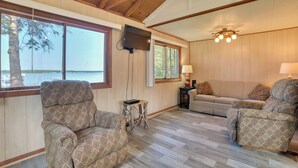 A spacious living area with a large window, a television mounted on the wall, and a cozy seating arrangement. - Mullett Lake Cabin w/ Private Dock & Fire Pit! (Indian River)