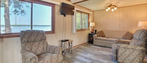 A spacious living area with a large window, a television mounted on the wall, and a cozy seating arrangement.