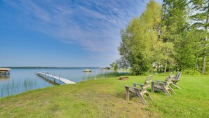 A lakeside setting with a dock extending into calm water, surrounded by grassy areas and trees. - Mullett Lake Cabin w/ Private Dock & Fire Pit! (Indian River)