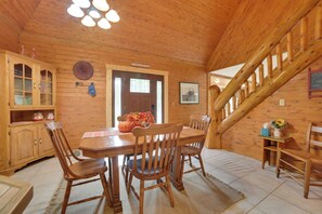 A wooden interior with a dining table, chairs, a staircase, and a kitchen area with cabinets and a window. - Fall Hikes & Fire Pit: Pet-friendly MI Retreat (Indian River)