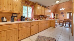 A spacious kitchen with wooden cabinets, a dining area with a table and chairs, and a large window with curtains. - Boat & Pet Friendly Home Near Mullett Lake (Indian River)
