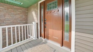 A wooden front door with a glass panel, a white porch railing, and a brick wall. - Boat & Pet Friendly Home Near Mullett Lake (Indian River)