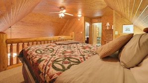 A cozy attic bedroom with a wooden ceiling, a bed with a quilt, a ceiling fan, and a view of the hallway. - Boat & Pet Friendly Home Near Mullett Lake (Indian River)