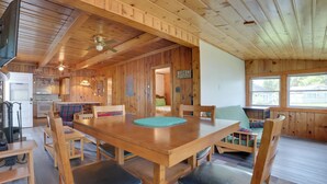 A wooden interior with a dining table, chairs, a kitchen area, and a view through large windows. - Waterfront Mullett Lake Cabin: Pets Welcome! (Indian River)