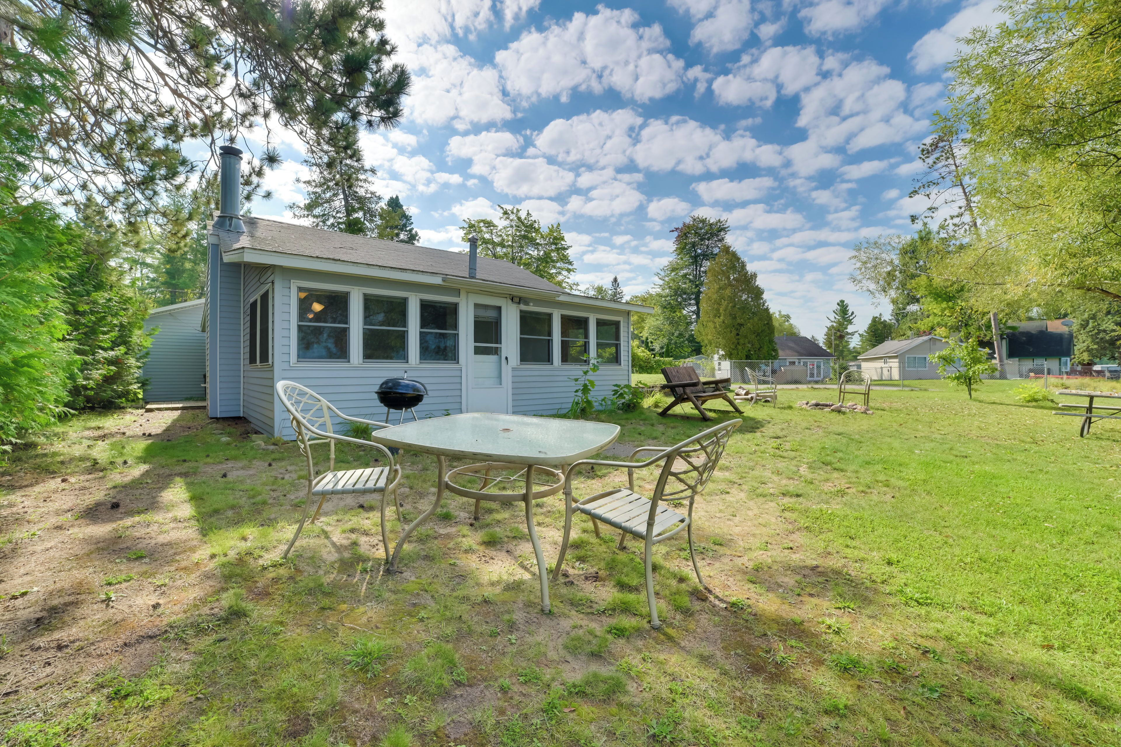 A small house with a covered patio, a grill, and a picnic table in a grassy yard.