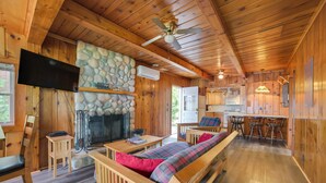 A cozy cabin interior with a stone fireplace, wooden furniture, a television, and a ceiling fan. - Waterfront Mullett Lake Cabin: Pets Welcome! (Indian River)