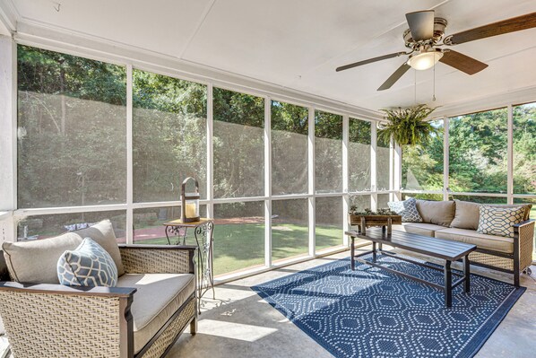 A sunroom with a large window, a ceiling fan, a sofa, a coffee table, and a rug.