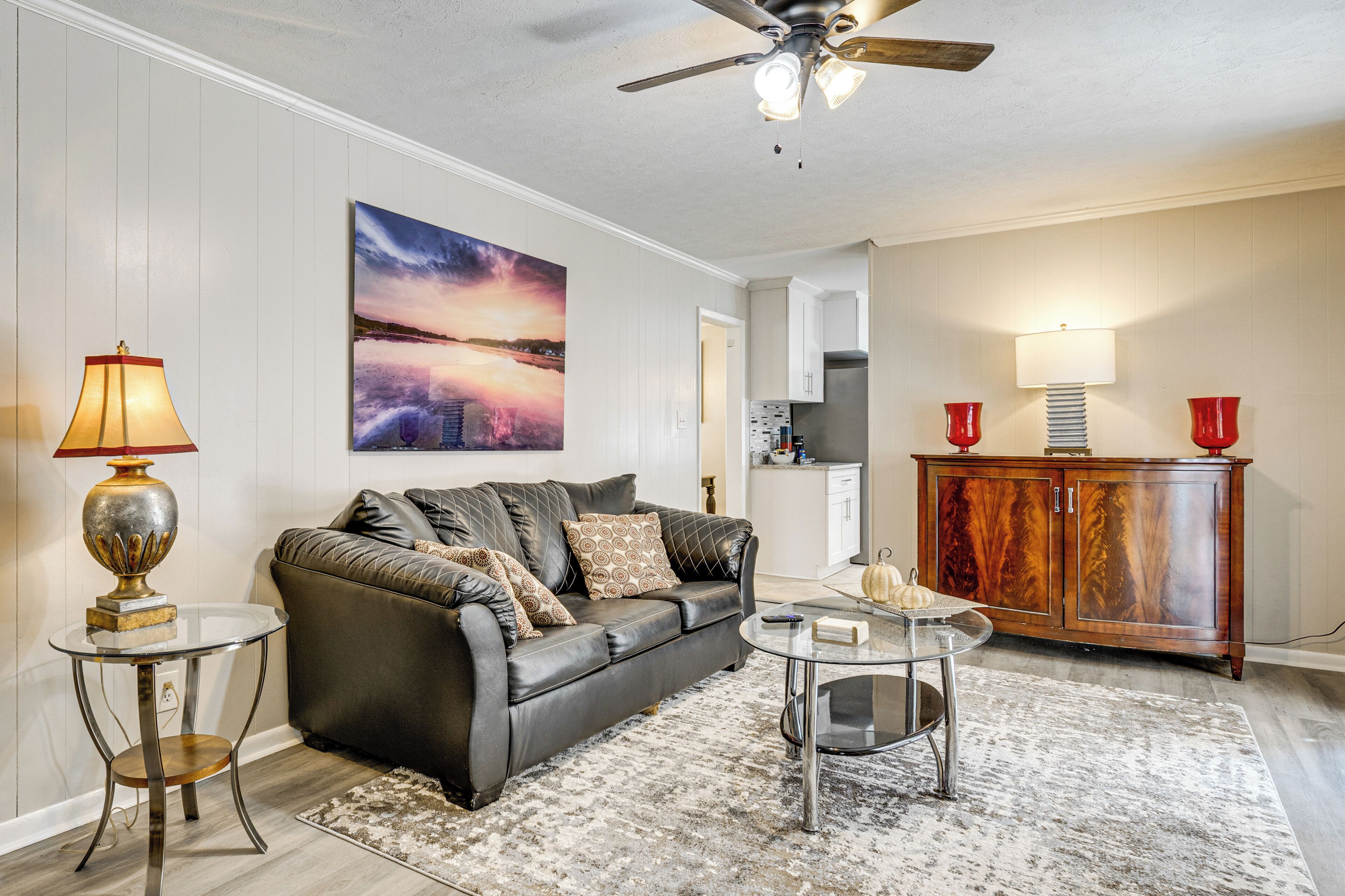 A living room with a leather sofa, a glass coffee table, a wooden cabinet, and a painting on the wall.