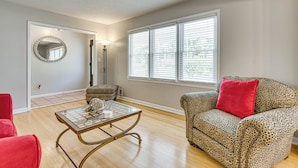 Un salon avec une table basse en verre, un canapé à motifs léopard agrémenté d’un coussin rouge, un fauteuil rouge, un pouf à motifs léopard et un miroir rond accroché au mur.