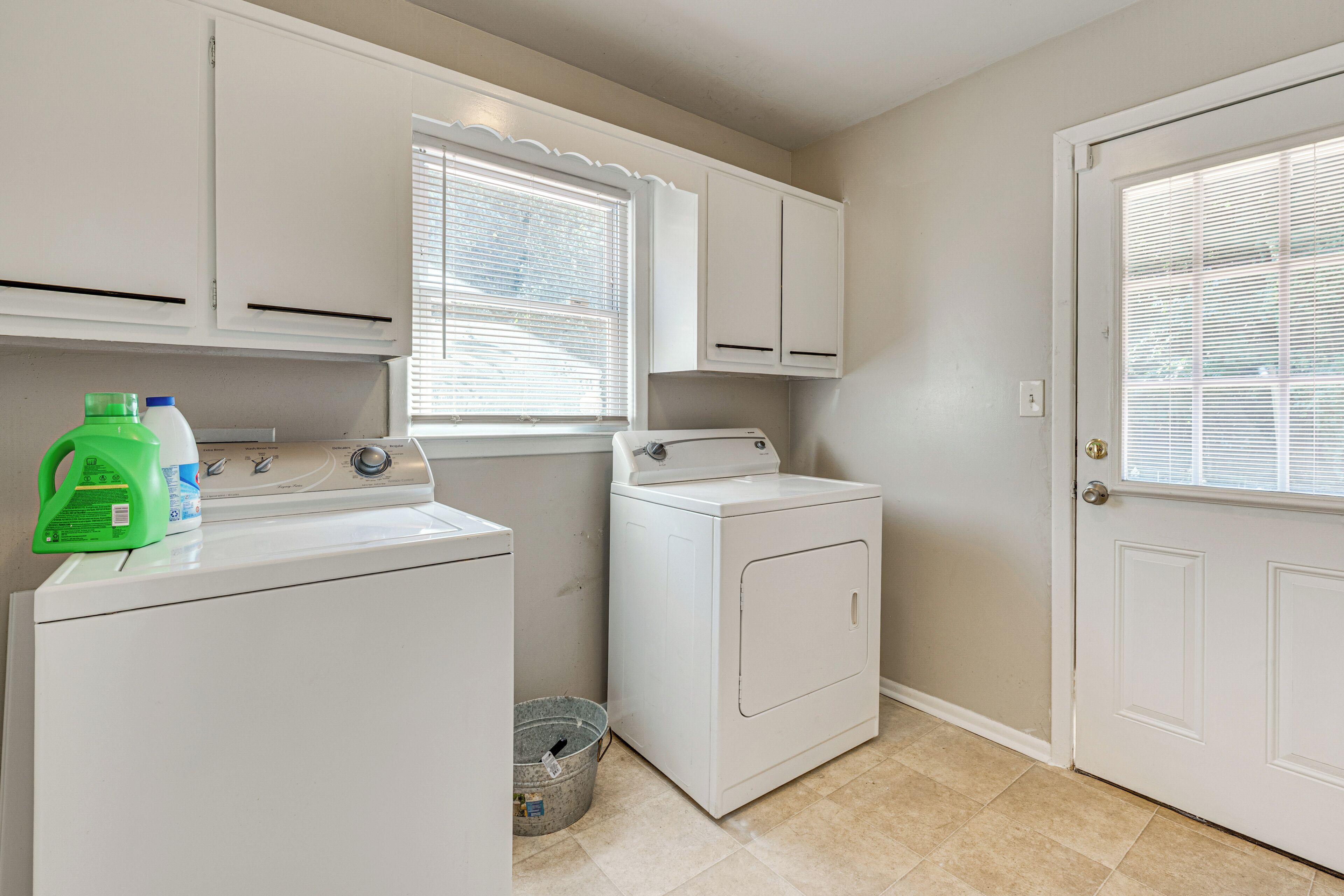 A laundry room with a washer, dryer, and a bucket.