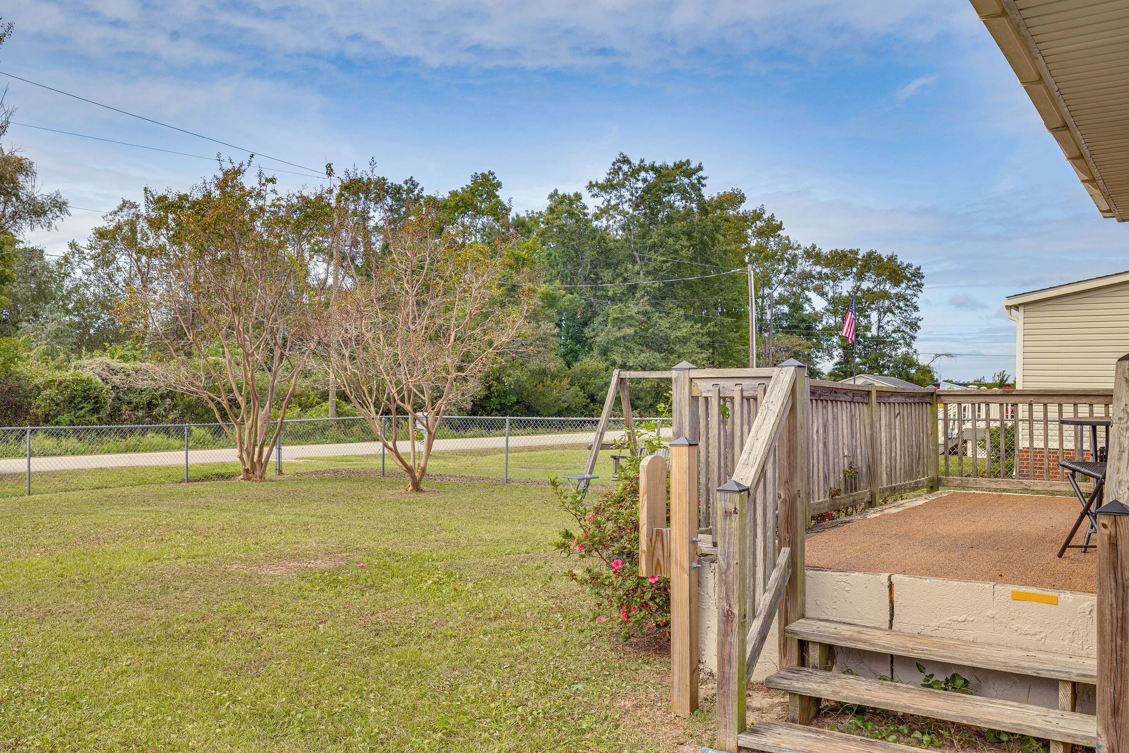 A fenced backyard with a wooden deck, a grassy area, and a building with a beige exterior.