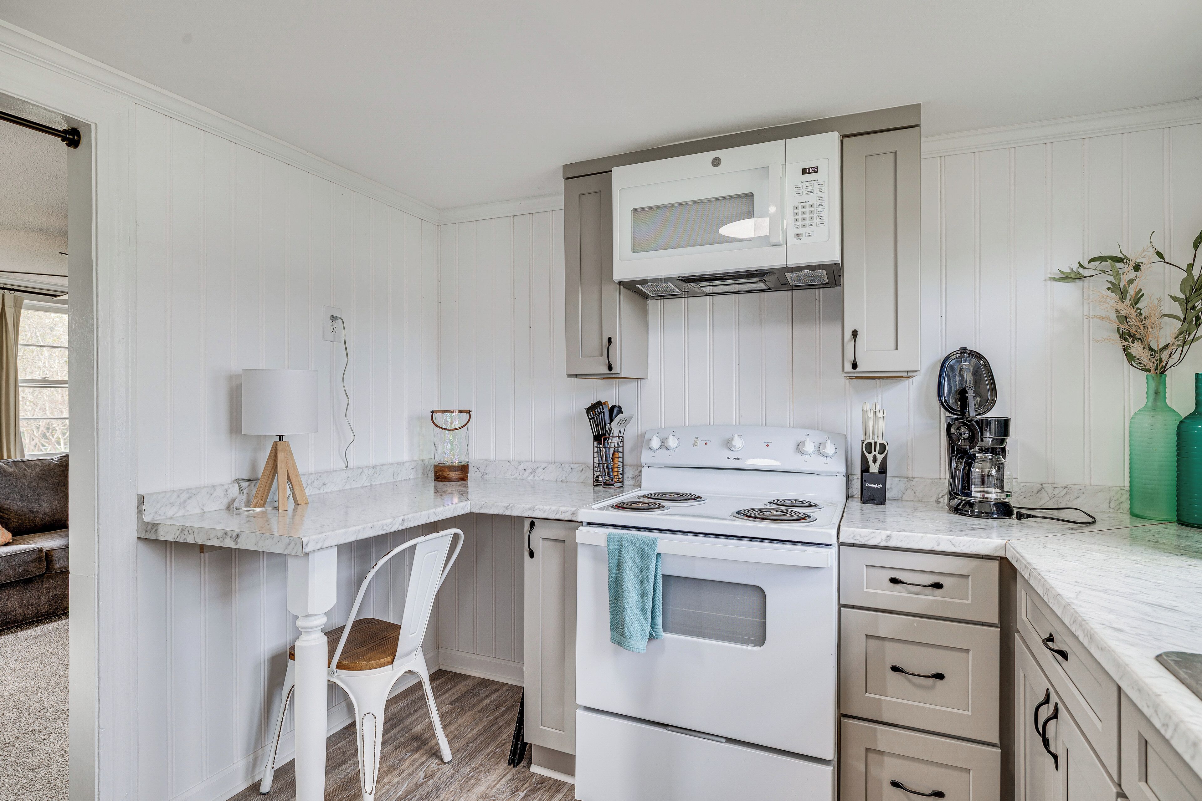 A compact kitchen with a white stove, microwave, and a small dining area with a chair and table.