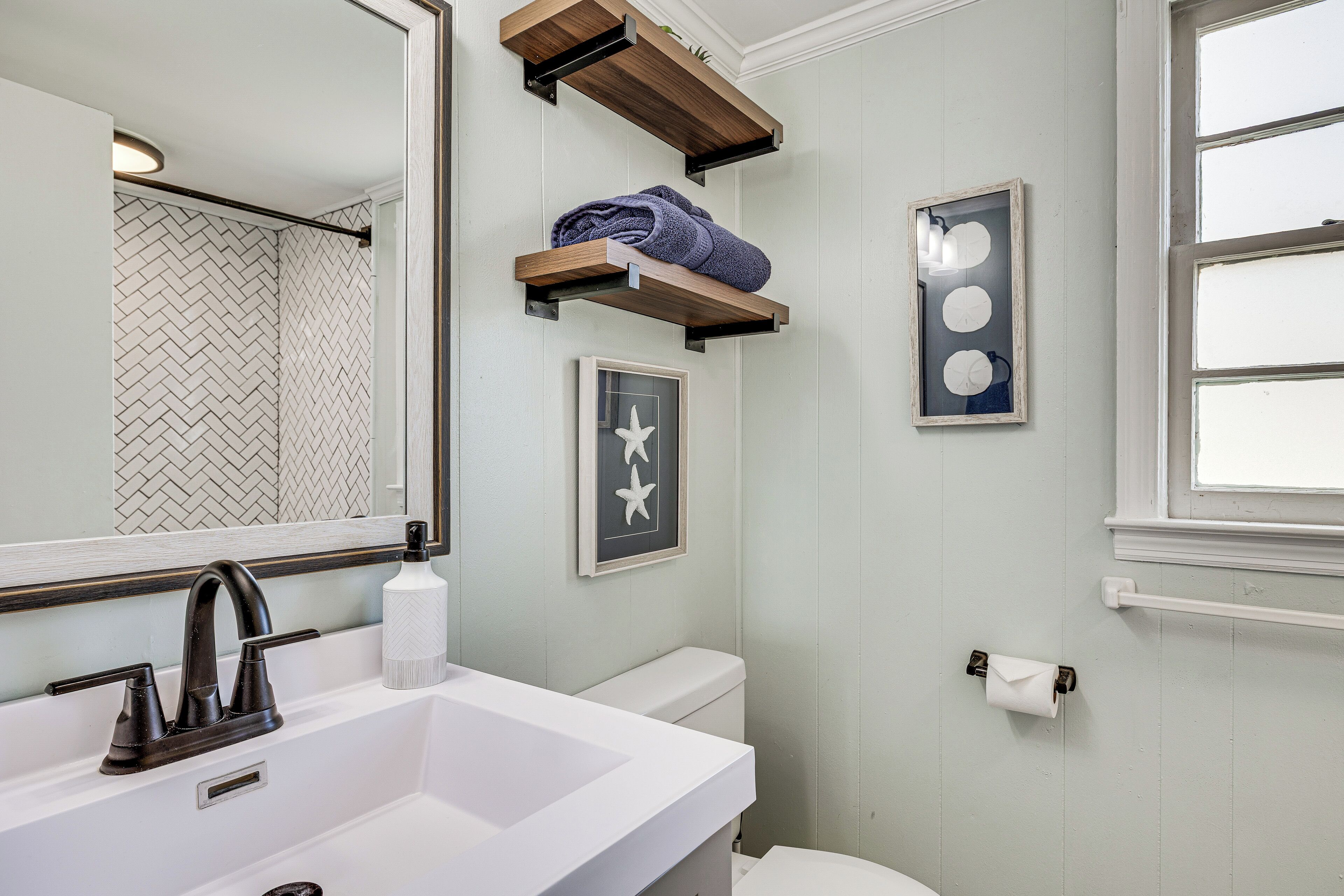 A bathroom with a white sink, a mirror, a toilet, and a window.