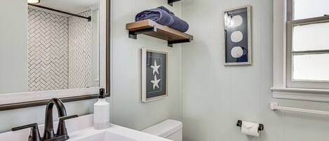 A bathroom with a white sink, a mirror, a toilet, and a window.