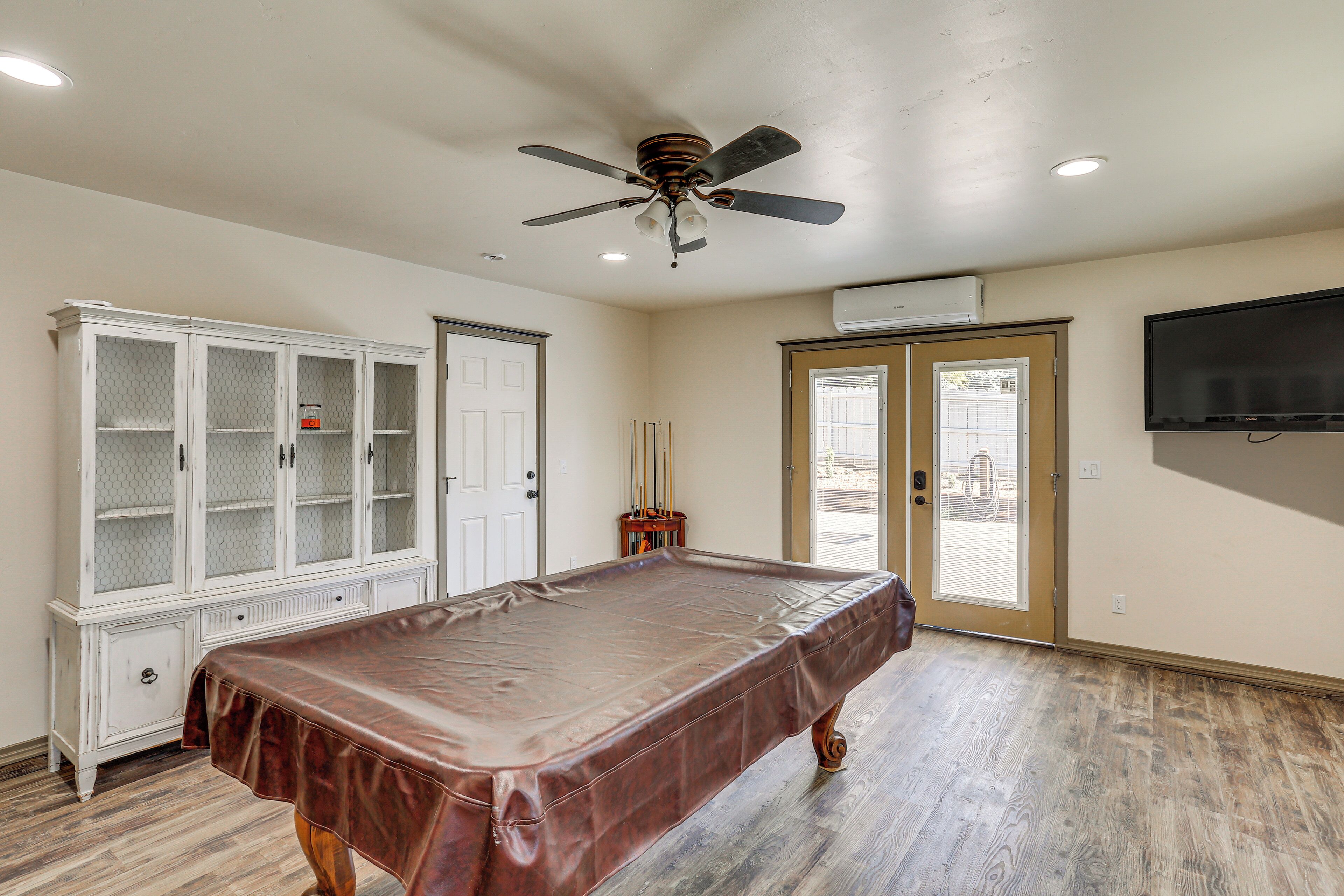 A pool table in a room with a ceiling fan, a cabinet, and a television mounted on the wall.