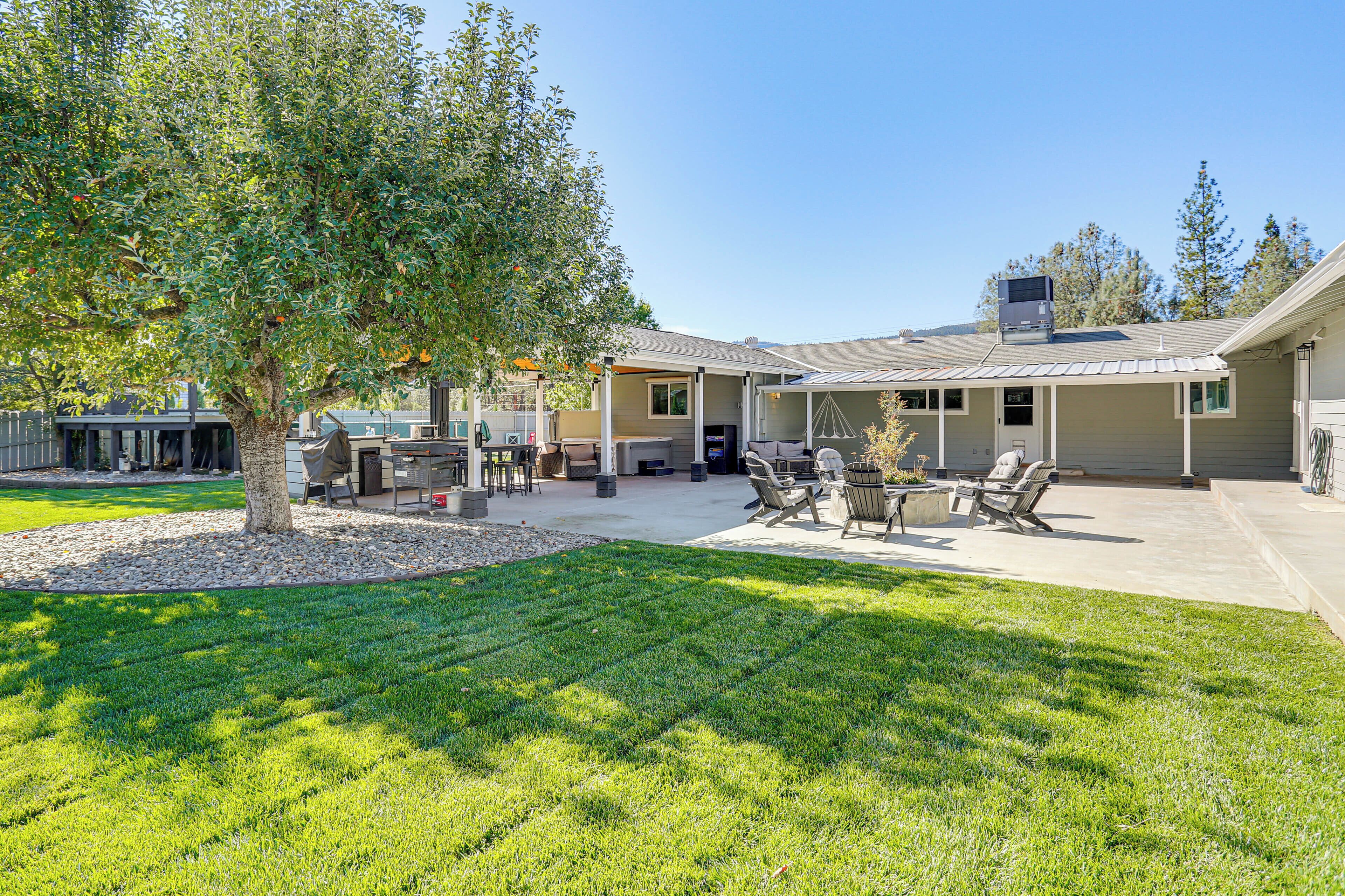 A covered outdoor patio with seating, a large tree, and a building with a flat roof.