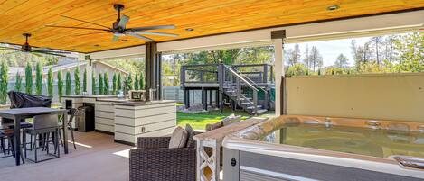 A covered outdoor area with a hot tub, seating, and a staircase leading to a deck.