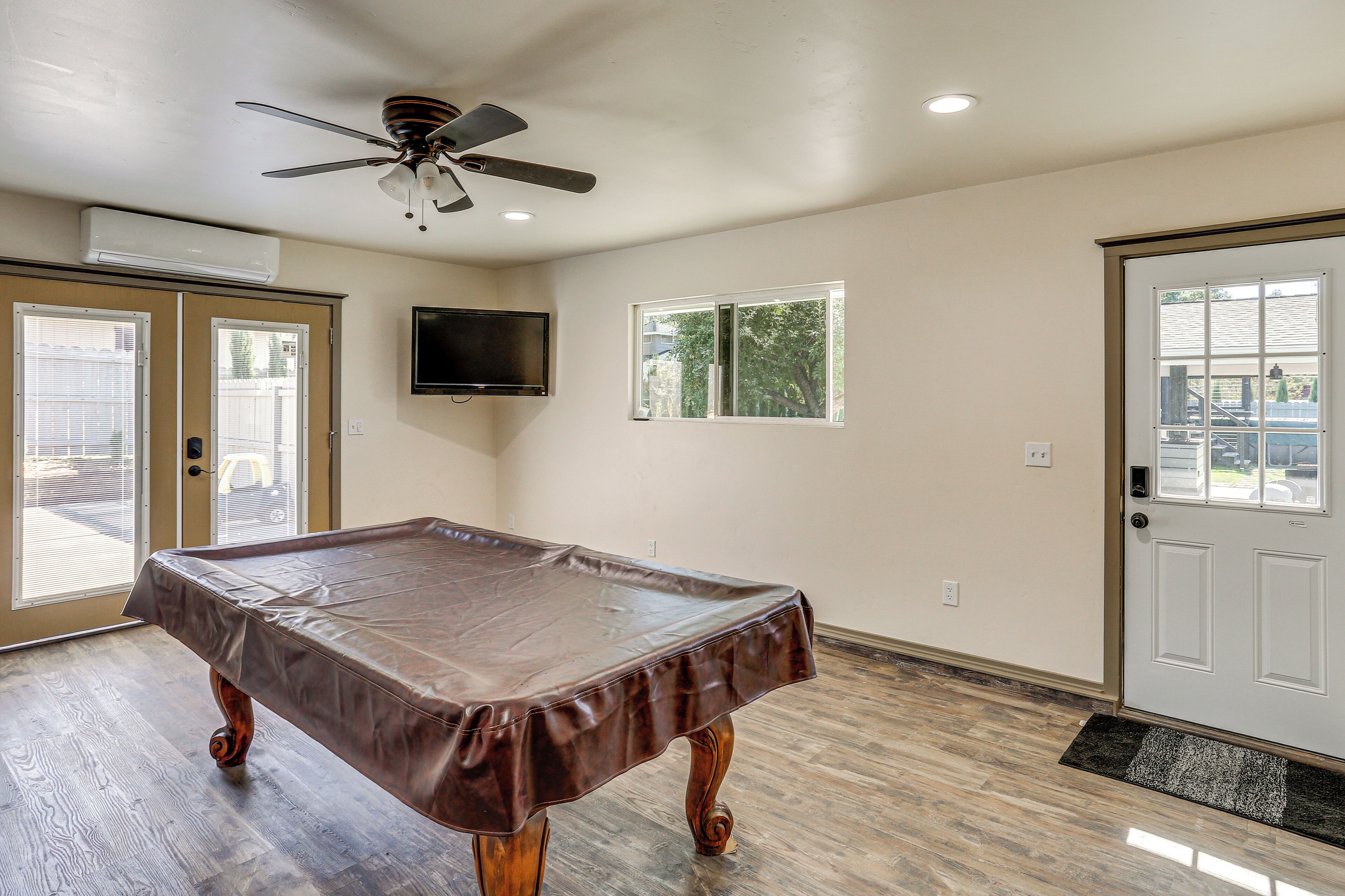 A pool table in a room with a ceiling fan, an air conditioning unit, a television, and a door with a window.