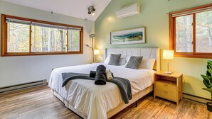A bedroom with a large bed, two bedside tables, a wall-mounted air conditioner, and a window with a view of trees. - Luxury Home w/ Game Room, 4 Mi to Bushkill Falls! (Bushkill)