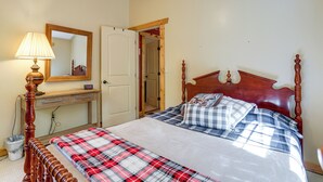 A bedroom with a bed, a wooden headboard, a bedside table with a lamp, a mirror, and a door leading to another room.