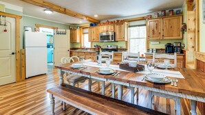 A spacious kitchen with wooden cabinets, a large wooden dining table set for six, and a refrigerator.