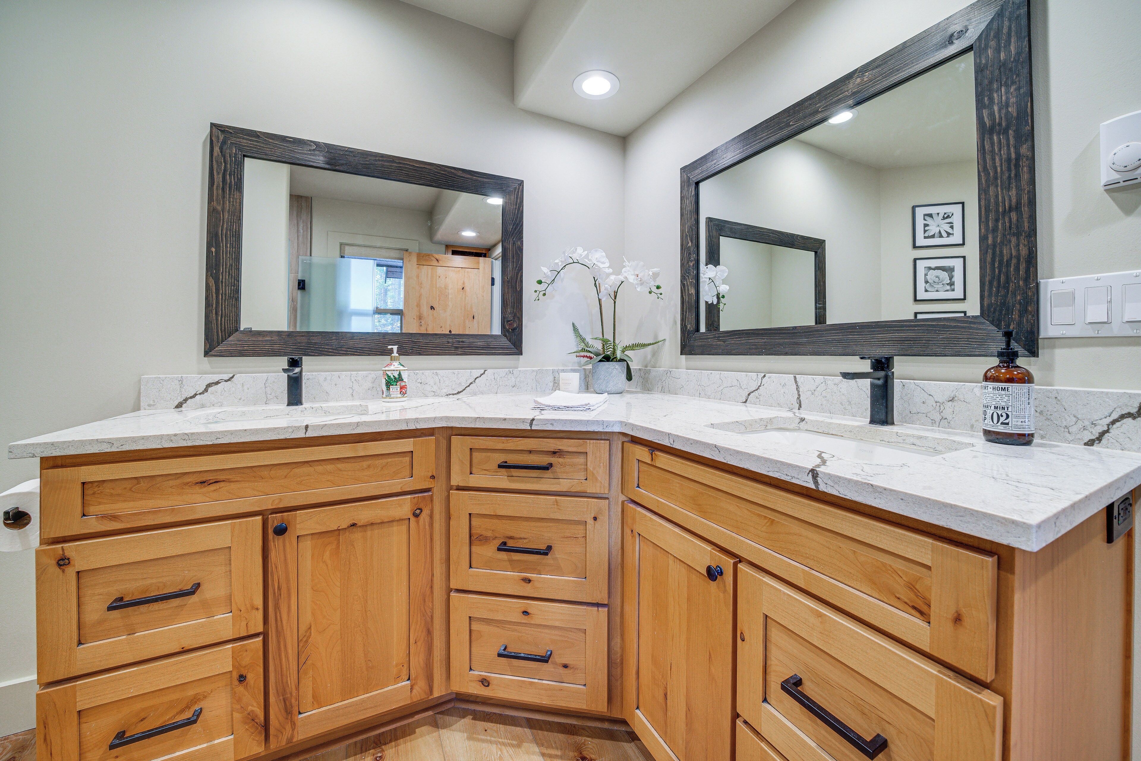 A bathroom with a corner sink, wooden cabinetry, marble countertops, and two large mirrors.