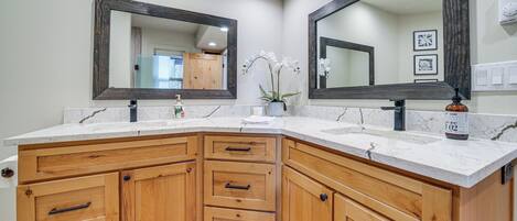 A bathroom with a corner sink, wooden cabinetry, marble countertops, and two large mirrors.