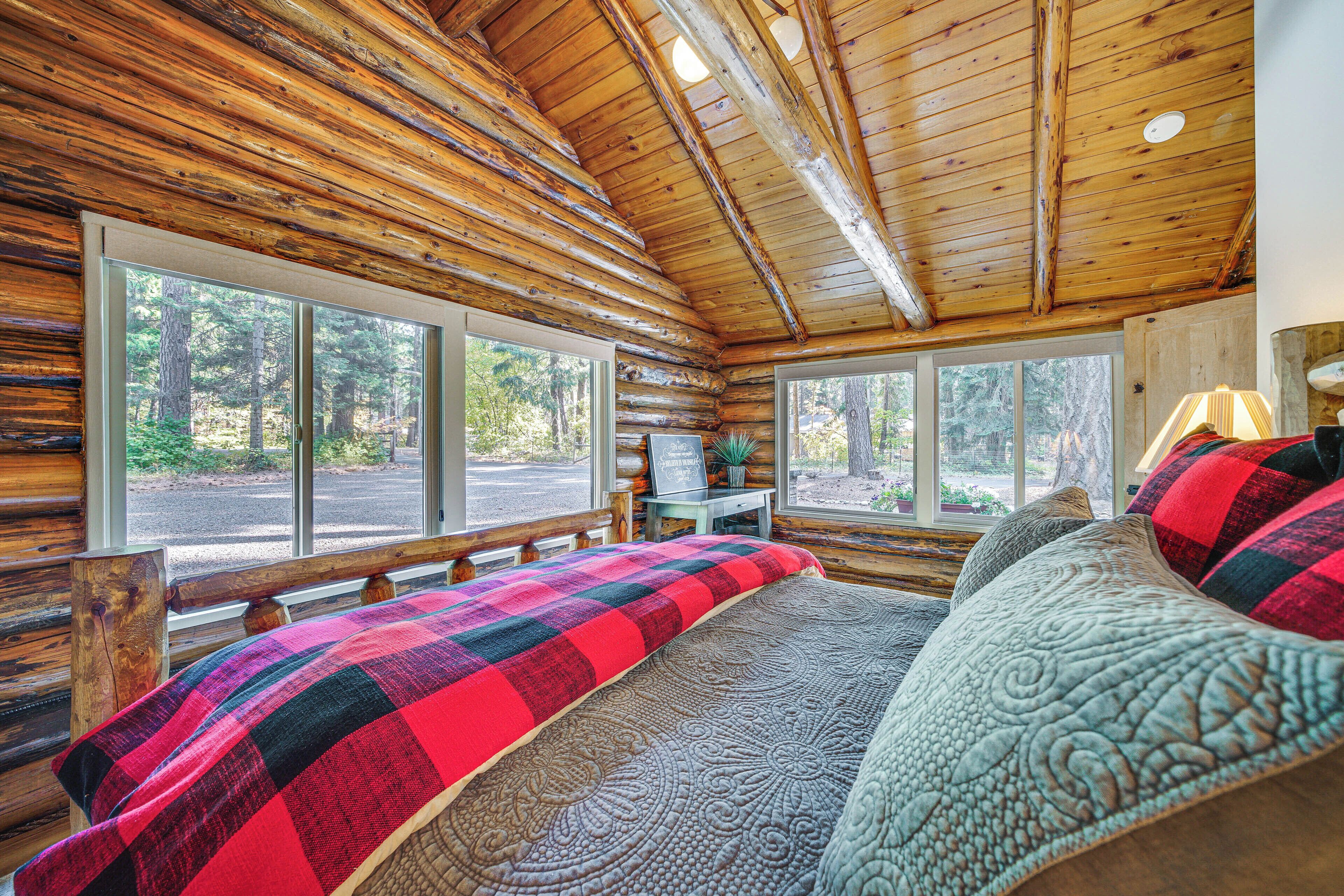 Une chambre située dans un chalet en rondins, avec un grand lit, deux fenêtres et une vue sur la forêt.