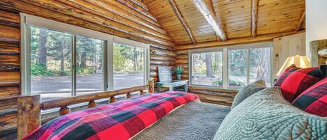 Une chambre située dans un chalet en rondins, avec un grand lit, deux fenêtres et une vue sur la forêt.