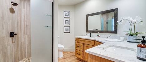 A modern bathroom with a glass shower enclosure, wooden vanity, and a large mirror.