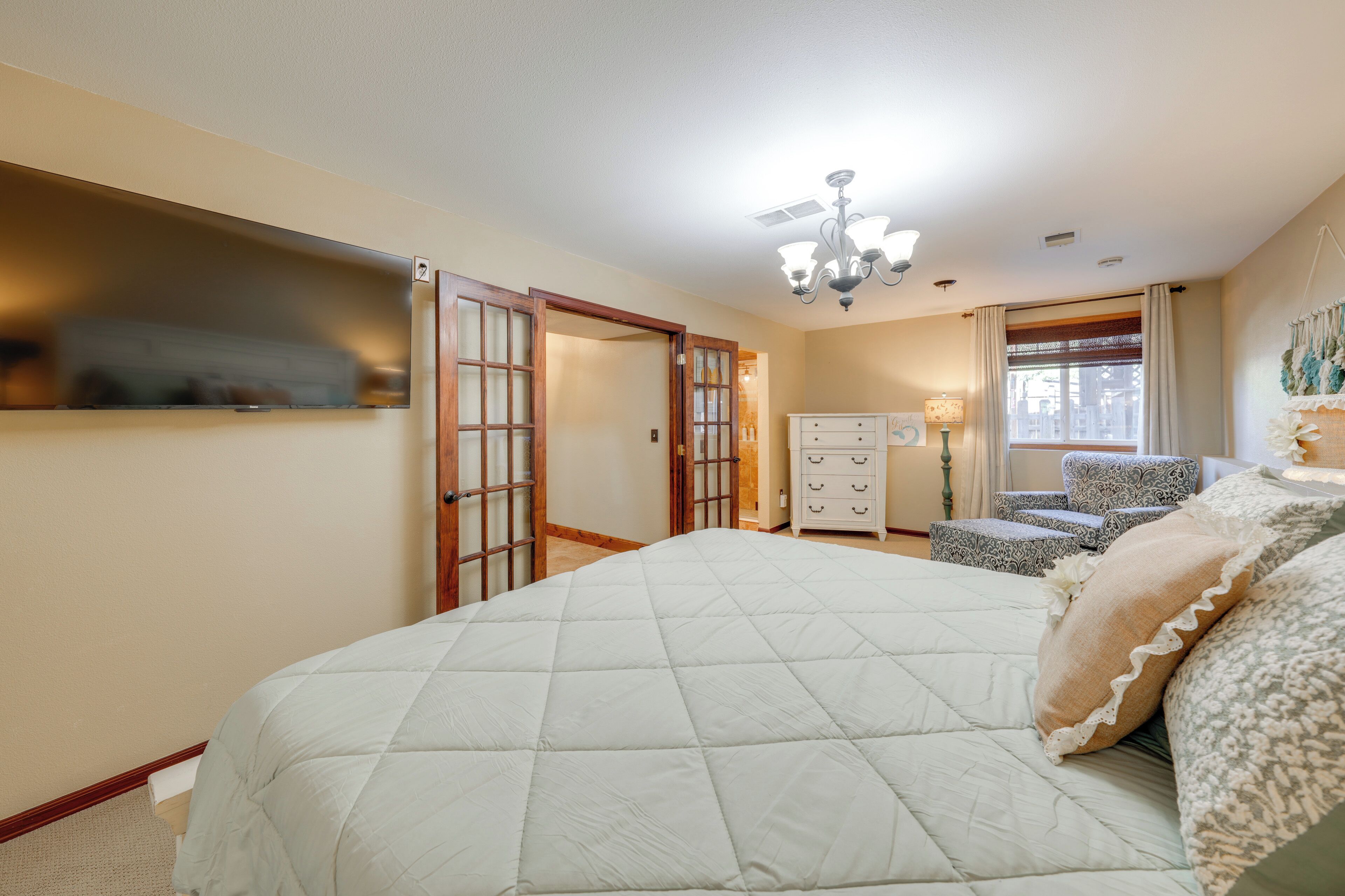 A bedroom with a large bed, a dresser, a chair, and a chandelier.