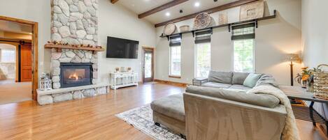 A spacious living room with a stone fireplace, wooden beams, and a large sofa.